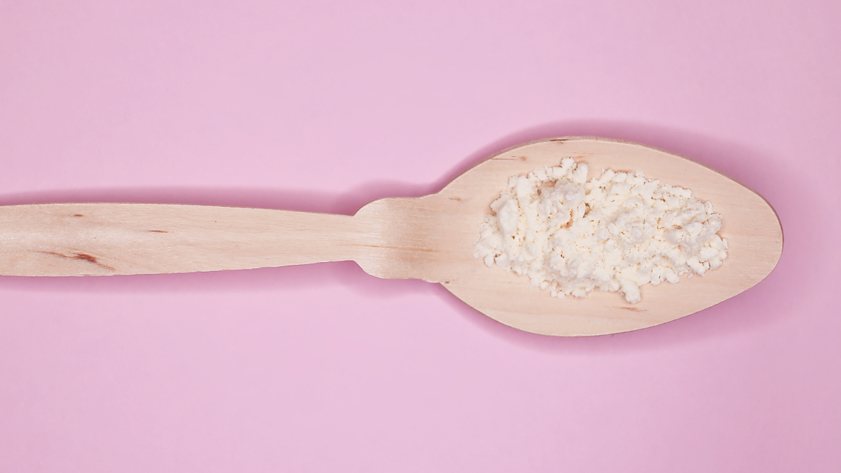 A spoonful of powdered colostrum on a pink background